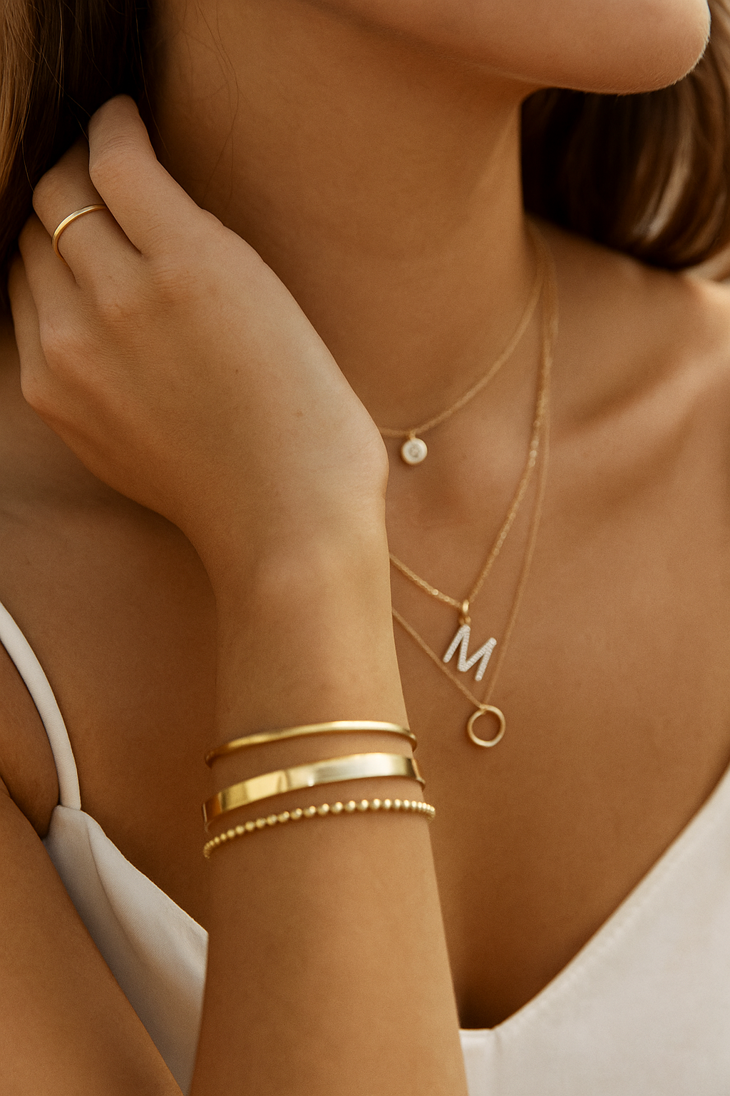 Close-up of a person wearing gold jewelry including necklaces, bracelets, and a ring.