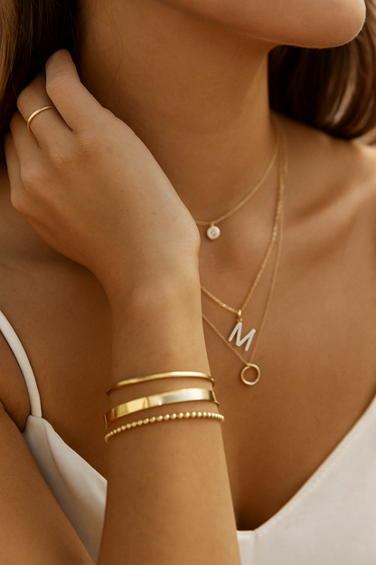 Close-up of a person wearing gold jewelry including necklaces, bracelets, and a ring.